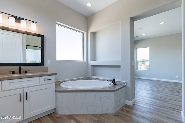 bathroom featuring hardwood / wood-style flooring, vanity, and tiled bath