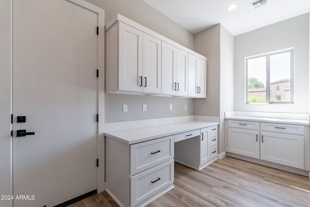 kitchen with light hardwood / wood-style flooring, white cabinets, light stone counters, and built in desk