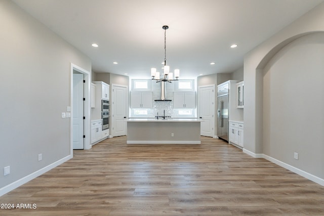 kitchen with white cabinetry, light hardwood / wood-style floors, tasteful backsplash, and an island with sink