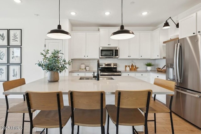 kitchen featuring white cabinetry, appliances with stainless steel finishes, a center island with sink, and decorative light fixtures