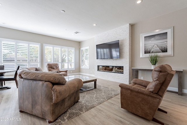 living room featuring a stone fireplace, wood finished floors, and a healthy amount of sunlight