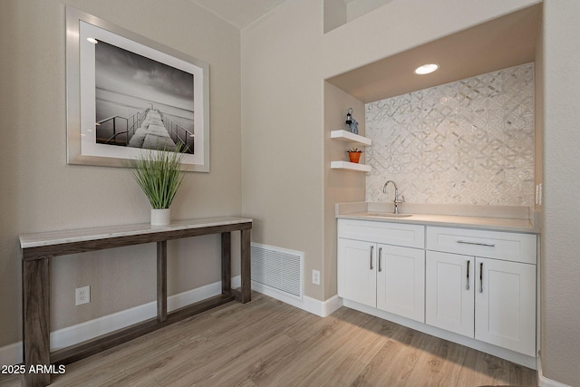 bar featuring visible vents, baseboards, light wood-style flooring, wet bar, and a sink