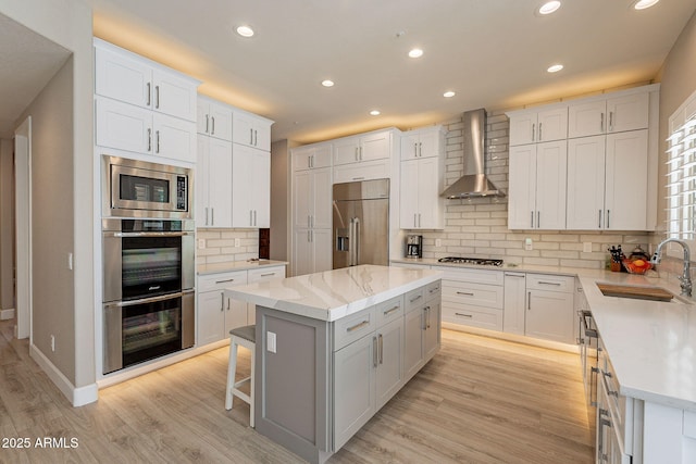 kitchen featuring a center island, appliances with stainless steel finishes, light wood-style floors, wall chimney exhaust hood, and a sink