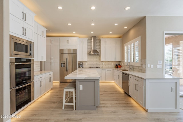 kitchen with plenty of natural light, stainless steel appliances, wall chimney range hood, and a sink