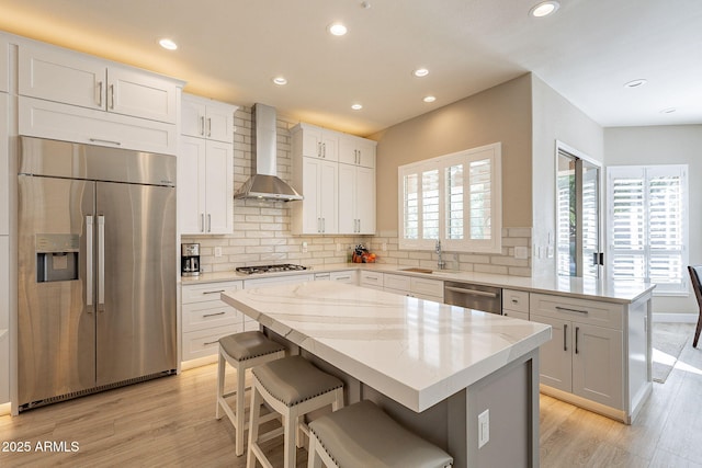 kitchen featuring a sink, backsplash, a center island, stainless steel appliances, and wall chimney range hood