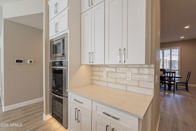 kitchen featuring baseboards, light wood-type flooring, appliances with stainless steel finishes, white cabinetry, and tasteful backsplash