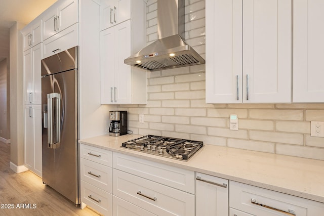 kitchen with light wood-style flooring, appliances with stainless steel finishes, white cabinets, wall chimney range hood, and decorative backsplash