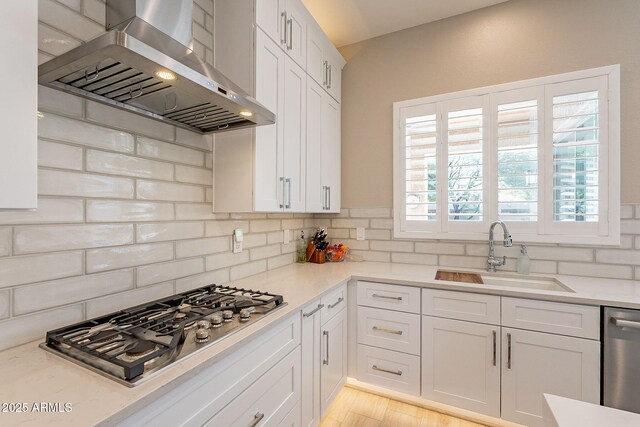 kitchen featuring a sink, white cabinets, appliances with stainless steel finishes, wall chimney exhaust hood, and tasteful backsplash