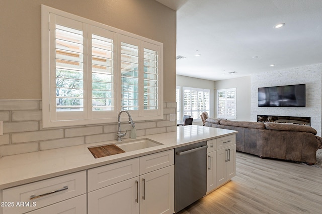 kitchen featuring a fireplace, a sink, white cabinets, light wood-style floors, and dishwasher