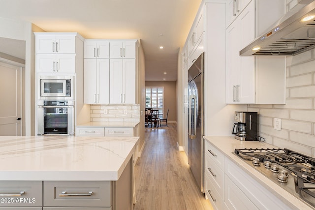 kitchen featuring light stone countertops, light wood-style floors, built in appliances, exhaust hood, and backsplash