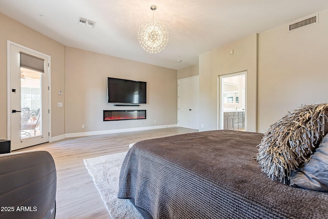 bedroom featuring visible vents, baseboards, light wood-style floors, and a glass covered fireplace