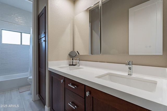 bathroom featuring double vanity, a sink, bathing tub / shower combination, toilet, and a textured wall