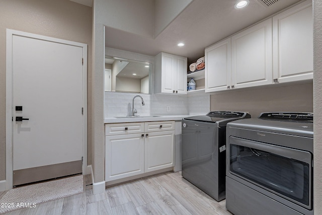 washroom with a sink, recessed lighting, cabinet space, light wood finished floors, and washing machine and clothes dryer