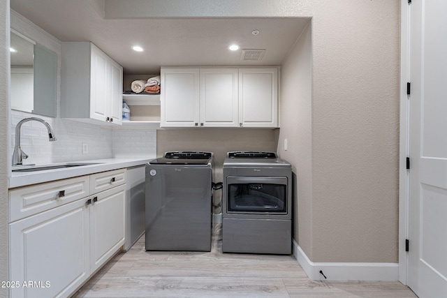 laundry area featuring baseboards, cabinet space, separate washer and dryer, a sink, and a textured wall