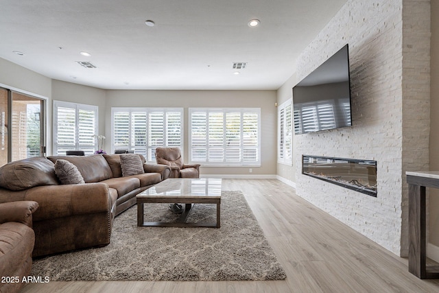 living room with visible vents, baseboards, a stone fireplace, and wood finished floors