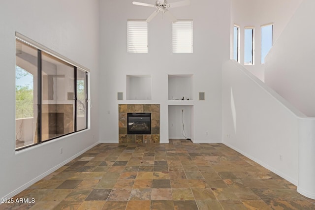 16600 N Thompson Peak Pkwy Unit 1072, Scottsdale, AZ 85260 - unfurnished living room featuring stone finish floor, baseboards, a fireplace, a towering ceiling, and a ceiling fan