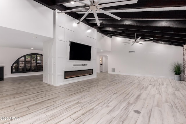 unfurnished living room with light wood-style flooring, a glass covered fireplace, a ceiling fan, and beam ceiling