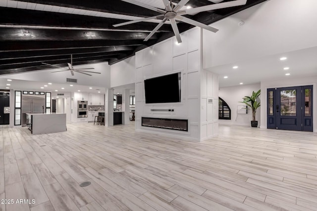 unfurnished living room featuring light wood-type flooring, beam ceiling, a glass covered fireplace, and a ceiling fan