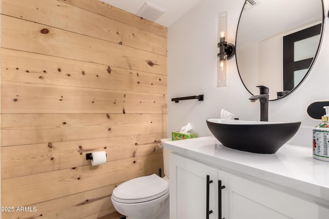 bathroom featuring toilet, vanity, and wood walls