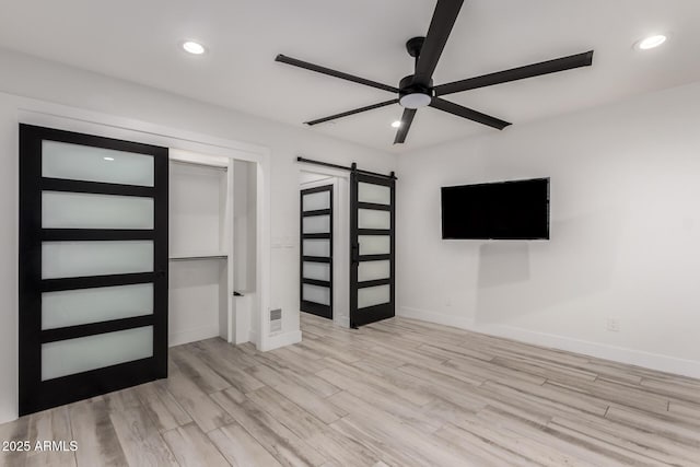 unfurnished bedroom featuring baseboards, a barn door, wood finished floors, and recessed lighting