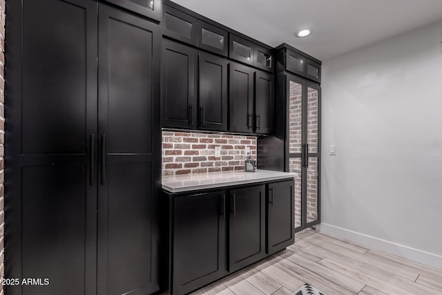 kitchen featuring light countertops, light wood finished floors, glass insert cabinets, baseboards, and dark cabinets