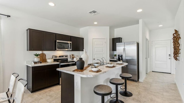 kitchen featuring stainless steel appliances, sink, a kitchen island with sink, a kitchen breakfast bar, and dark brown cabinets