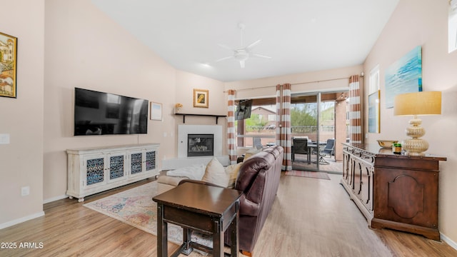 living room with wood finished floors, ceiling fan, a glass covered fireplace, and baseboards
