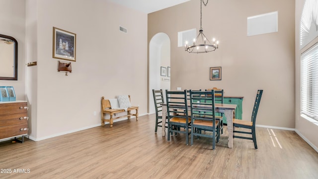 dining room featuring a high ceiling, wood finished floors, a chandelier, arched walkways, and plenty of natural light