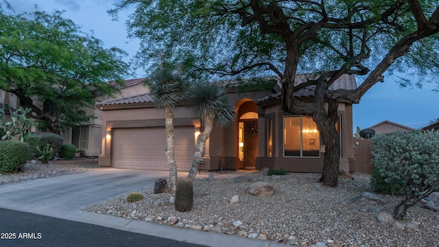 mediterranean / spanish house with a garage, stucco siding, concrete driveway, and a tiled roof