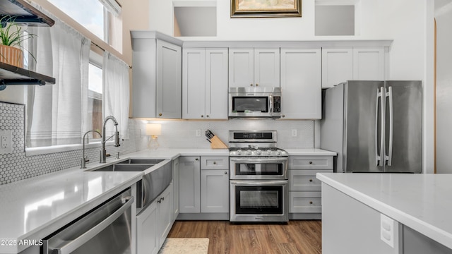 kitchen with appliances with stainless steel finishes, tasteful backsplash, wood finished floors, light countertops, and a sink