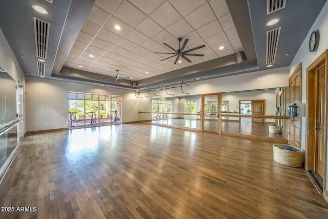 workout area with a tray ceiling, ceiling fan, wood finished floors, and baseboards