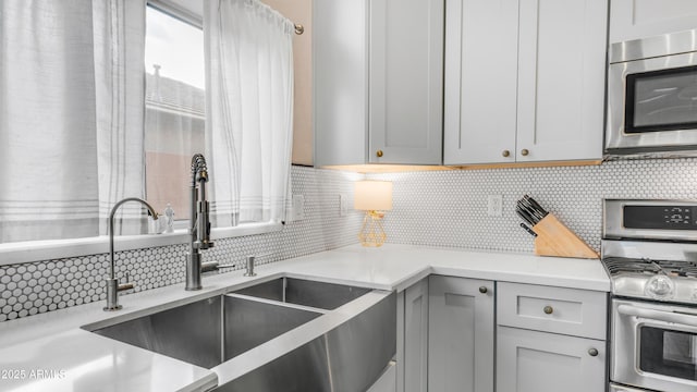 kitchen with stainless steel appliances, a sink, tasteful backsplash, and light countertops