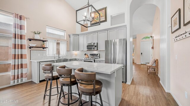 kitchen featuring stainless steel appliances, high vaulted ceiling, gray cabinetry, open shelves, and light wood-style floors