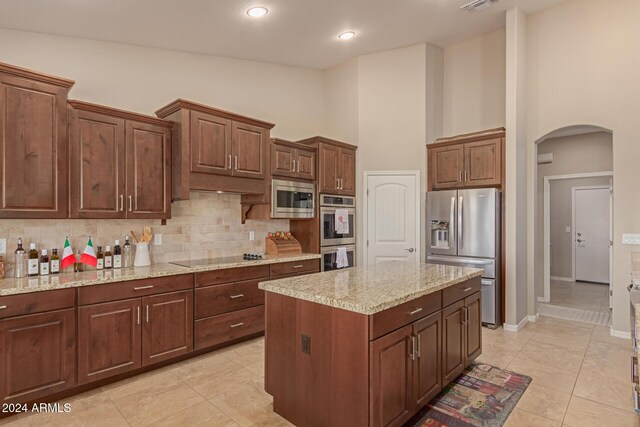 kitchen with light tile patterned flooring, high vaulted ceiling, light stone countertops, appliances with stainless steel finishes, and a kitchen island