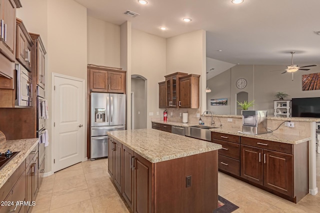 kitchen with appliances with stainless steel finishes, light stone counters, sink, high vaulted ceiling, and a kitchen island