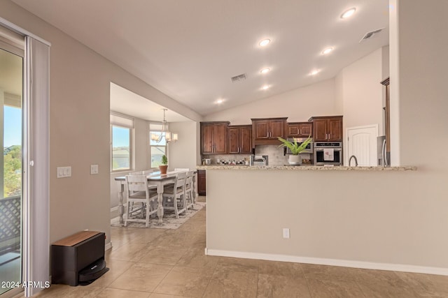 kitchen with kitchen peninsula, appliances with stainless steel finishes, light stone counters, vaulted ceiling, and a notable chandelier