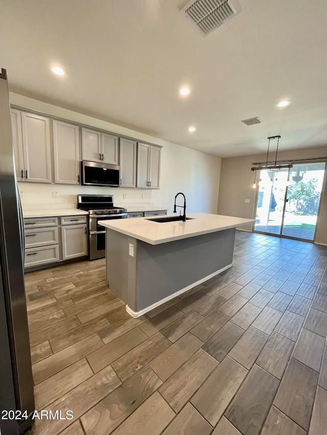 kitchen featuring appliances with stainless steel finishes, sink, light wood-type flooring, an island with sink, and pendant lighting