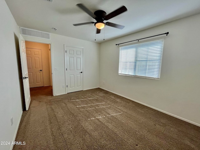 unfurnished bedroom with a closet, dark carpet, and ceiling fan