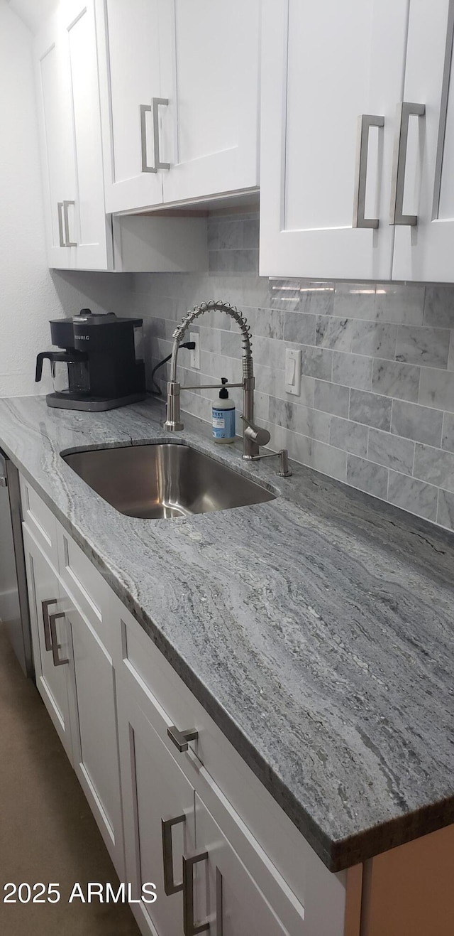 kitchen with white cabinetry, light stone countertops, and sink