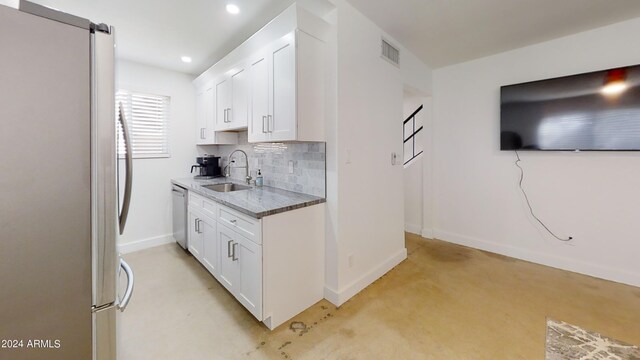 kitchen featuring sink, white cabinetry, stone countertops, stainless steel appliances, and backsplash