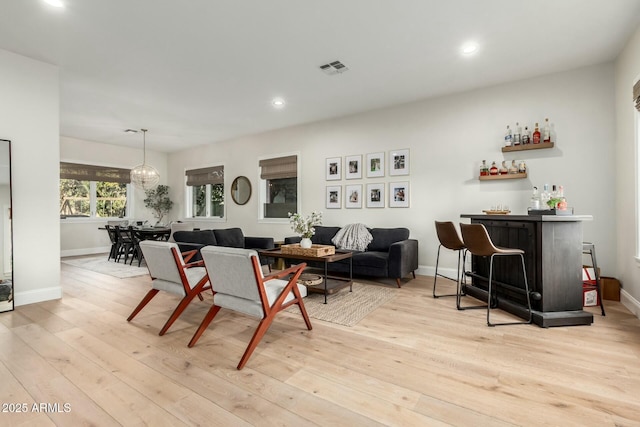 dining area with a notable chandelier, bar area, and light wood-type flooring