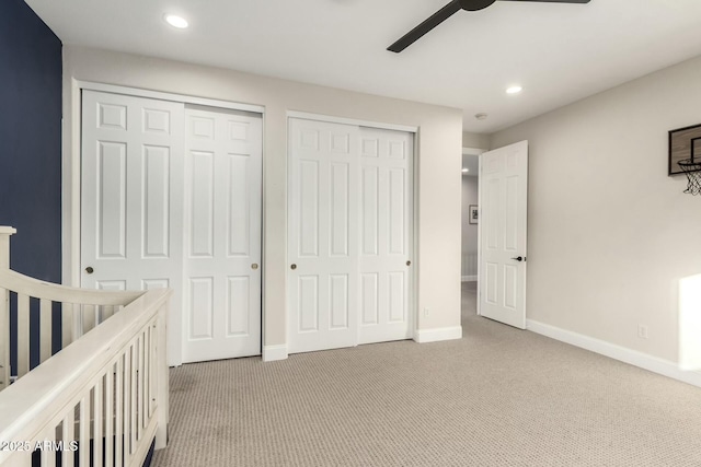 unfurnished bedroom featuring ceiling fan, light colored carpet, and two closets