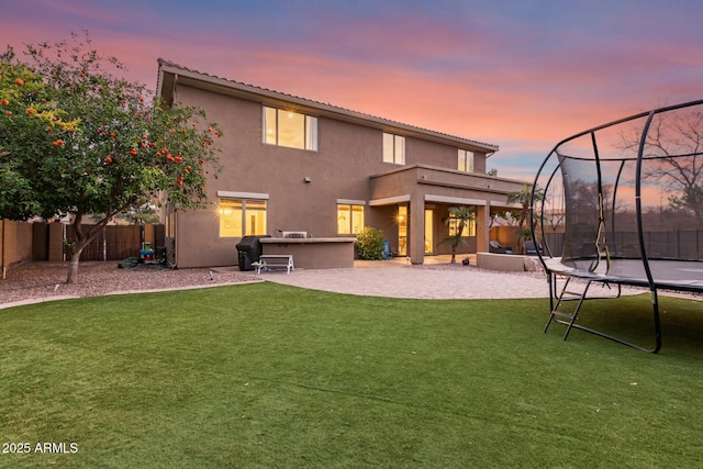 back house at dusk featuring a balcony, a patio area, a trampoline, and a lawn