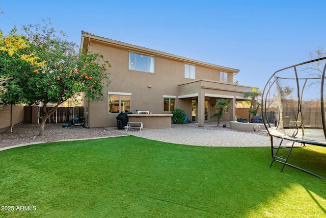 rear view of property featuring a trampoline, a yard, a patio area, and a balcony