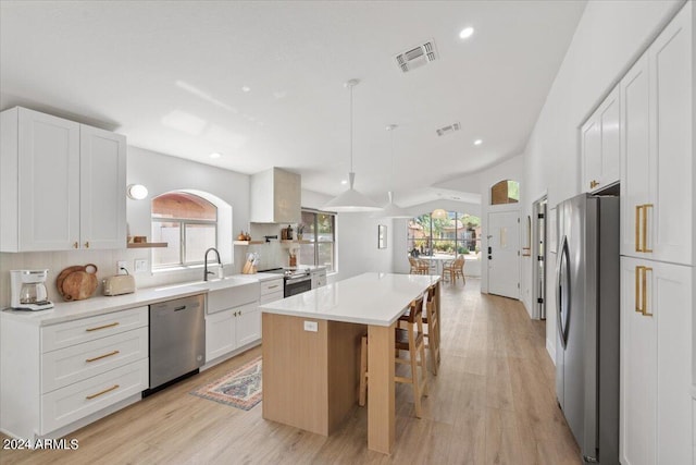 kitchen with pendant lighting, a center island, backsplash, white cabinetry, and stainless steel appliances