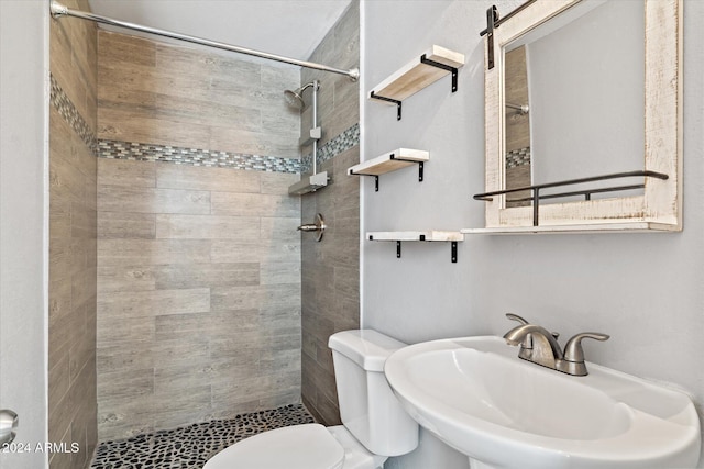 bathroom with tiled shower, toilet, and sink