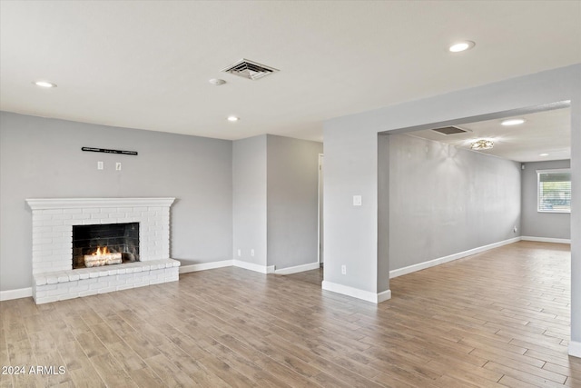 unfurnished living room featuring light wood-type flooring and a brick fireplace