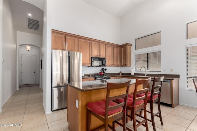 kitchen featuring a kitchen island, a towering ceiling, dark countertops, visible vents, and appliances with stainless steel finishes