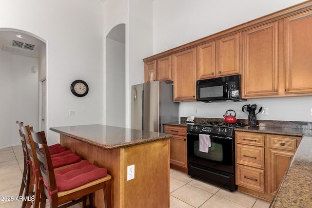 kitchen featuring a breakfast bar area, brown cabinetry, light tile patterned floors, visible vents, and black appliances