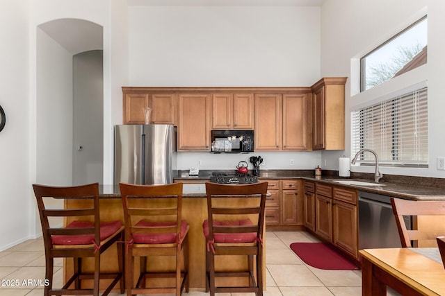 kitchen with light tile patterned floors, a towering ceiling, a sink, and stainless steel appliances